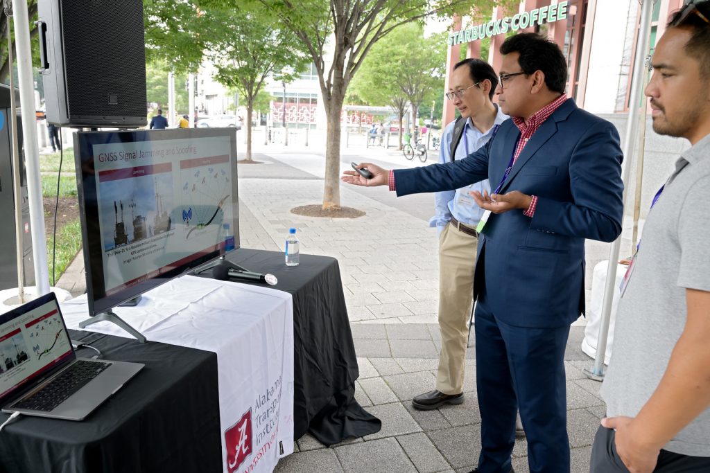 A man in a suit points to a screen as onlookers listen to his explanation.