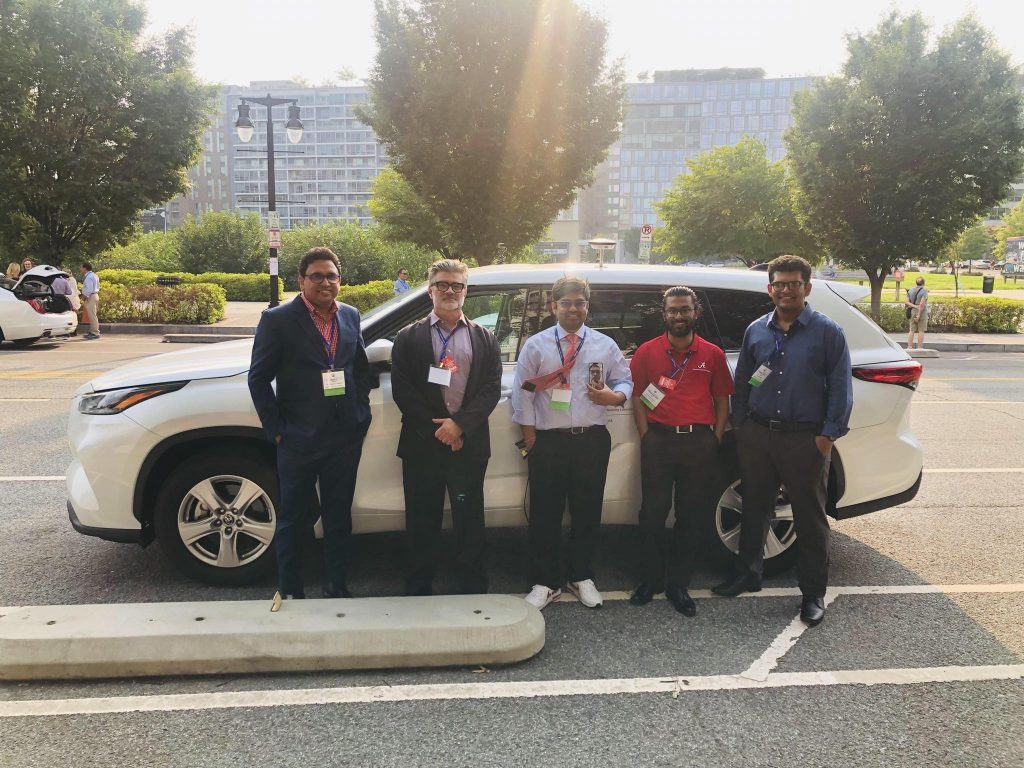 Five men standing in front of the live outdoor demonstration vehicle.